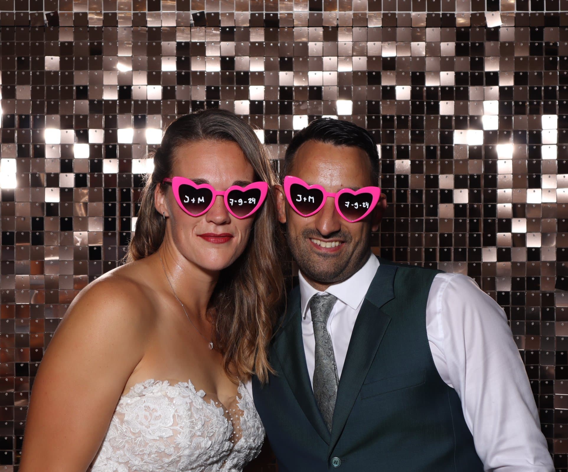 Couple de mariés avec lunettes cœur devant un fond à paillettes